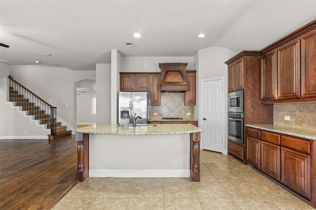 kitchen featuring visible vents, an island with sink, appliances with stainless steel finishes, light stone counters, and a sink