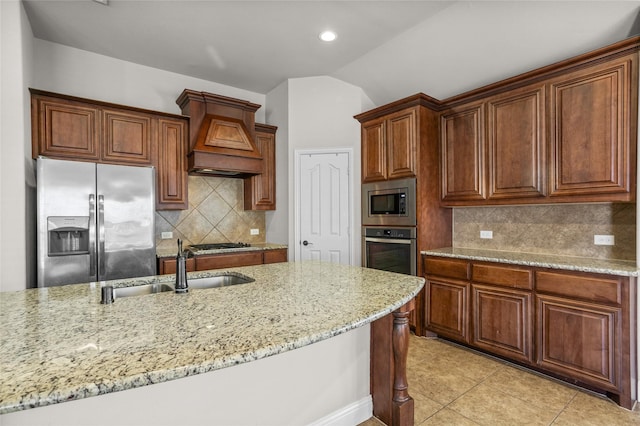 kitchen with custom range hood, light stone counters, appliances with stainless steel finishes, vaulted ceiling, and a sink