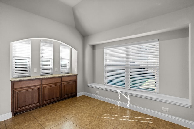 spare room with vaulted ceiling, baseboards, and light tile patterned floors