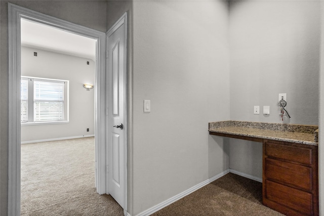 hallway featuring baseboards and dark colored carpet