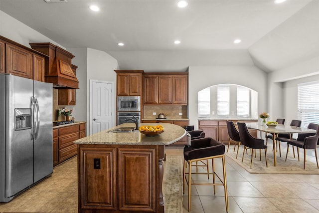 kitchen with light stone counters, a center island with sink, lofted ceiling, backsplash, and appliances with stainless steel finishes