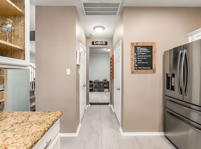 interior space featuring light stone countertops, visible vents, stainless steel fridge with ice dispenser, and white cabinetry