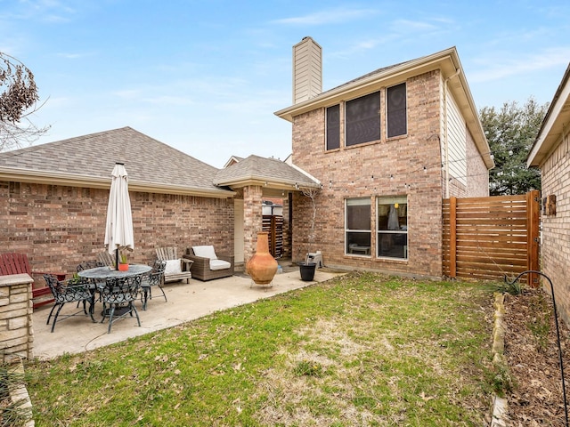 rear view of house with a patio, brick siding, fence, a yard, and a chimney