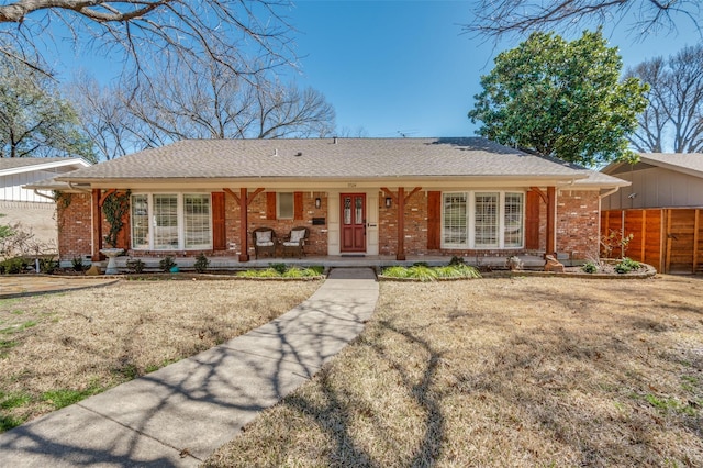 single story home featuring covered porch, a shingled roof, fence, and brick siding