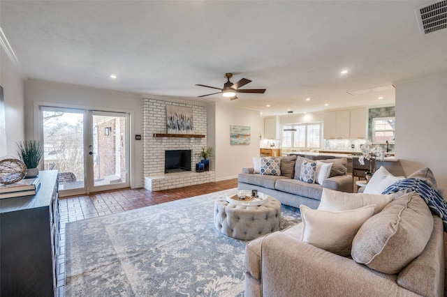 living area featuring recessed lighting, visible vents, baseboards, a brick fireplace, and crown molding