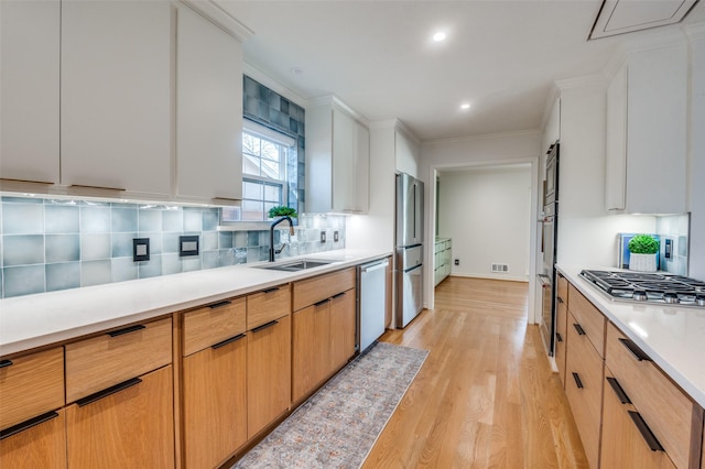 kitchen featuring stainless steel appliances, light countertops, decorative backsplash, light wood-style floors, and a sink