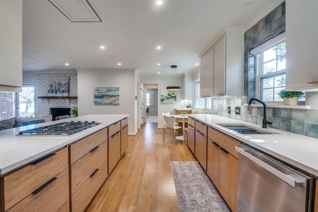 kitchen with light wood finished floors, tasteful backsplash, appliances with stainless steel finishes, light countertops, and a sink