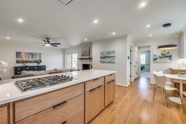 kitchen featuring crown molding, light wood finished floors, light countertops, stainless steel gas stovetop, and open floor plan