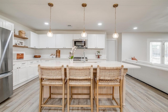 kitchen featuring light wood-style flooring, stainless steel appliances, a breakfast bar, visible vents, and open shelves