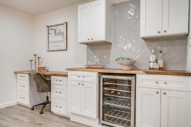 bar featuring wine cooler, tasteful backsplash, light wood-style floors, a bar, and baseboards