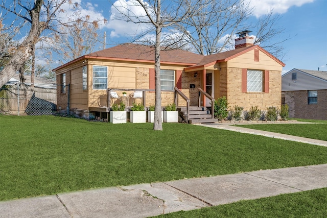 view of front facade with brick siding, a chimney, fence, and a front yard