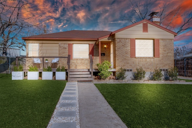 view of front facade with a yard, brick siding, a chimney, and fence