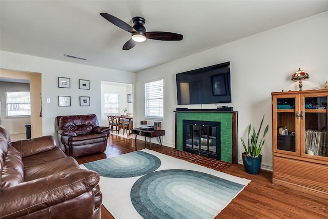 living room with a fireplace with flush hearth, wood finished floors, visible vents, and a healthy amount of sunlight