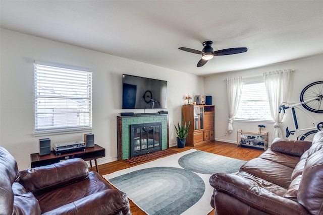 living area featuring a ceiling fan, a fireplace, baseboards, and wood finished floors