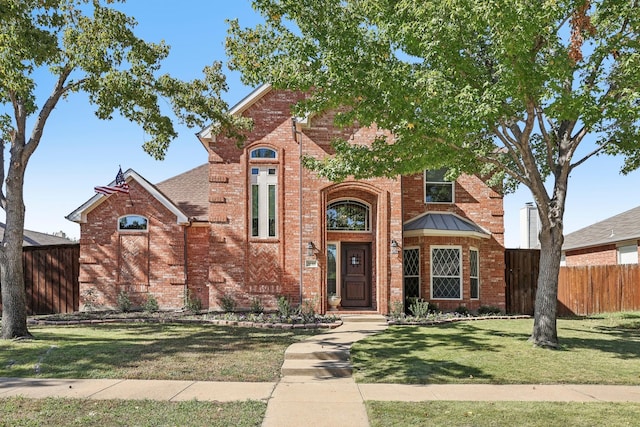 traditional-style house featuring a front yard, fence, and brick siding