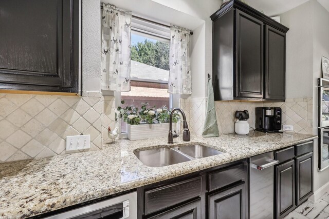 kitchen featuring dishwashing machine, light stone counters, backsplash, and a sink