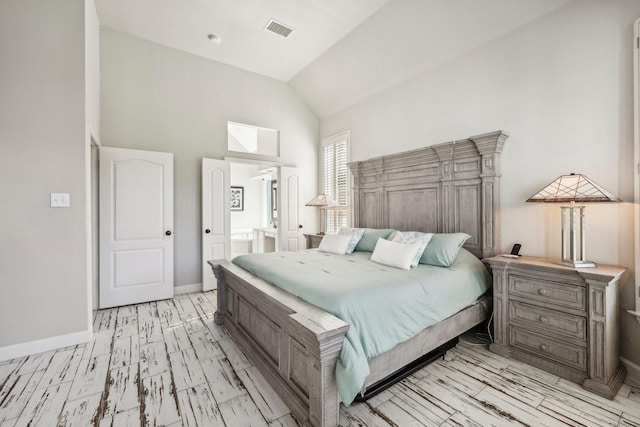 bedroom with high vaulted ceiling, visible vents, light wood-style floors, baseboards, and ensuite bath