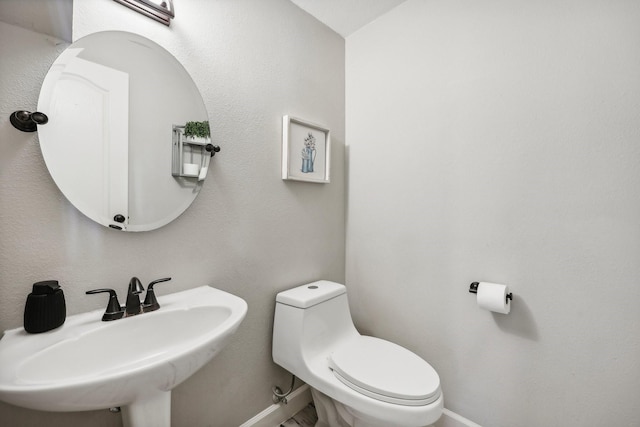 half bathroom with baseboards, a sink, and toilet