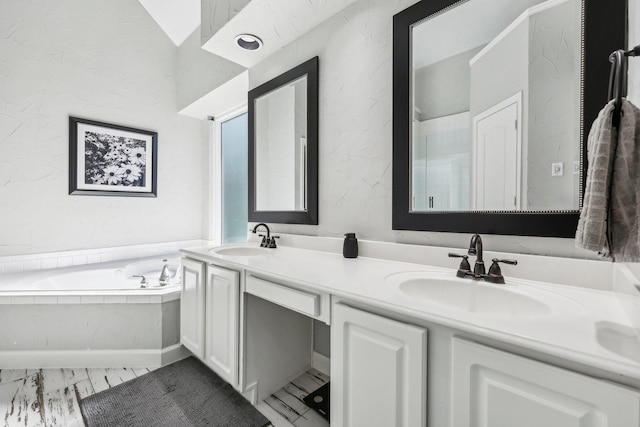 bathroom featuring a textured wall, double vanity, a sink, and a bath