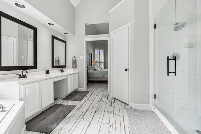 ensuite bathroom with a sink, baseboards, vaulted ceiling, double vanity, and a stall shower