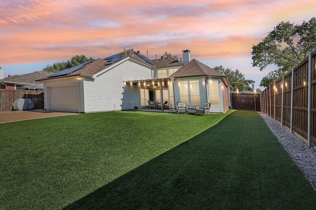 rear view of house with a patio, solar panels, a lawn, an attached garage, and a fenced backyard