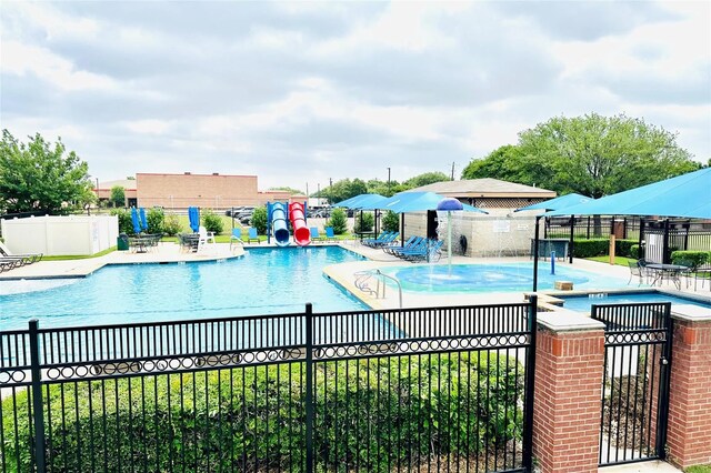 community pool with a water slide, a patio area, fence, and a water play area