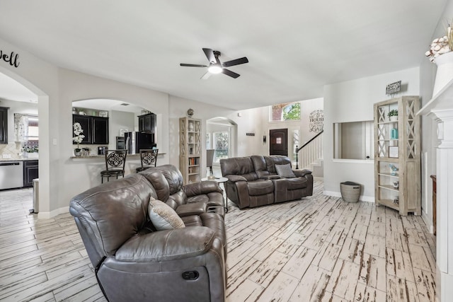 living area with baseboards, arched walkways, a ceiling fan, light wood-style flooring, and stairs