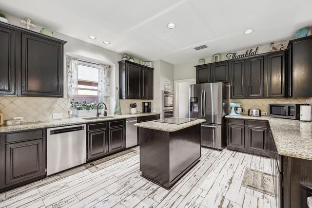 kitchen with light stone counters, a center island, stainless steel appliances, visible vents, and a sink