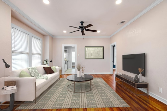 living area with ornamental molding, visible vents, baseboards, and wood finished floors