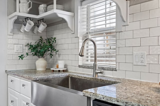 kitchen featuring light stone counters, white cabinetry, backsplash, and a sink