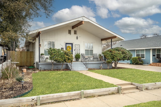 bungalow with a front yard, covered porch, fence, and concrete driveway