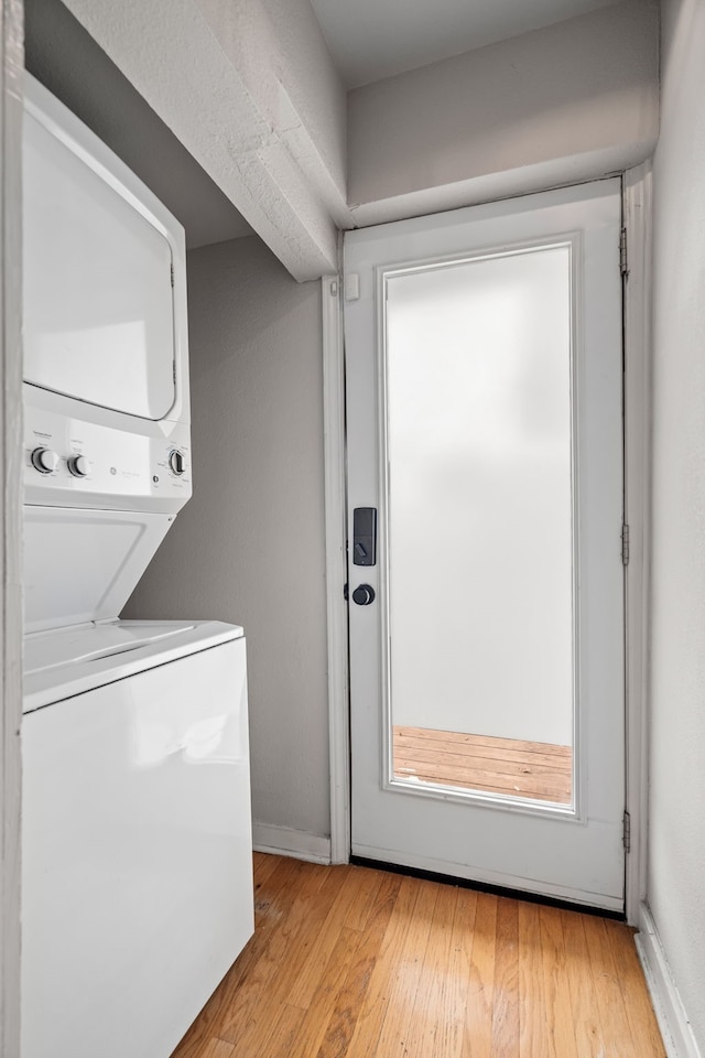 washroom featuring stacked washer and dryer, laundry area, light wood-style floors, and baseboards