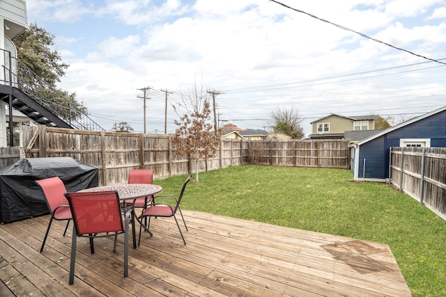 deck with outdoor dining area, a fenced backyard, and a lawn