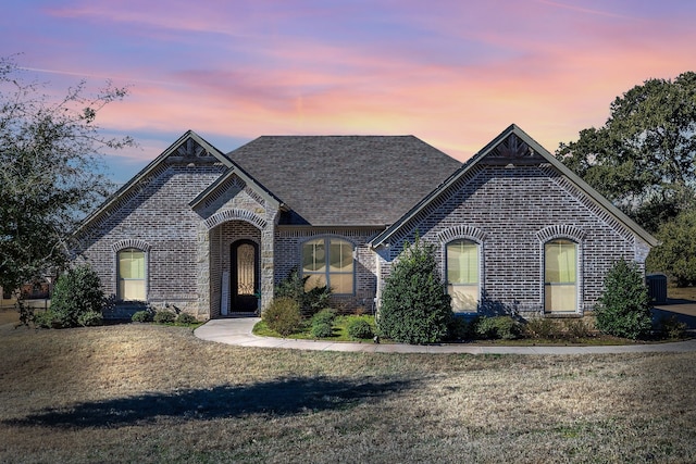 french provincial home with brick siding, a front lawn, and roof with shingles