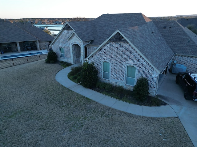 french provincial home with a shingled roof, fence, a front lawn, and brick siding