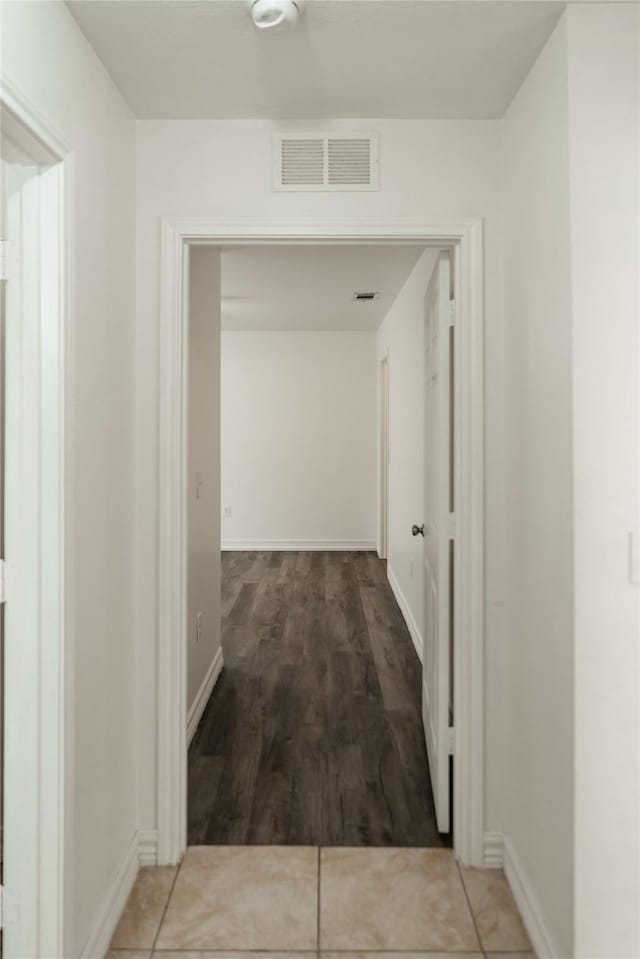 corridor featuring visible vents, baseboards, and wood finished floors