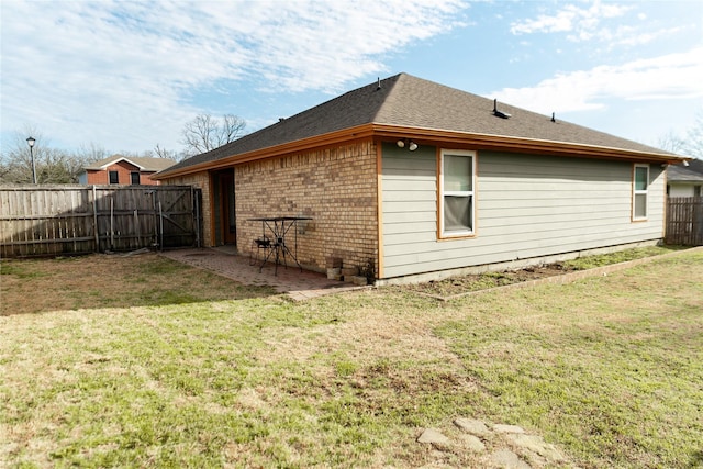 view of side of property featuring roof with shingles, brick siding, a lawn, a patio area, and fence