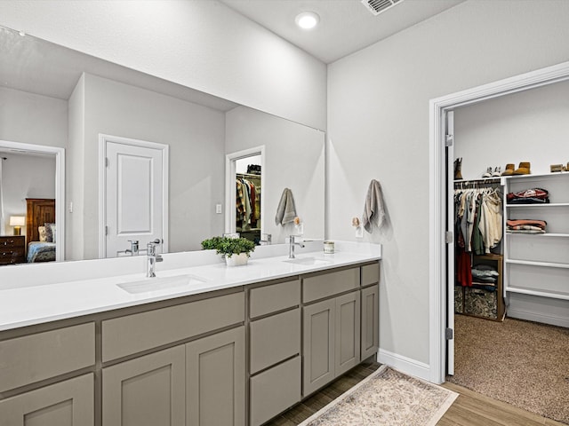 ensuite bathroom with double vanity, connected bathroom, a sink, and wood finished floors