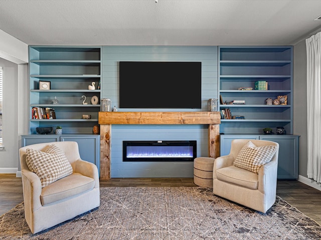 living room with a textured ceiling, built in shelves, wood finished floors, baseboards, and a glass covered fireplace