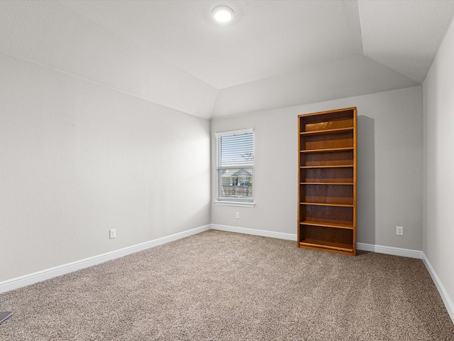 carpeted spare room featuring lofted ceiling and baseboards