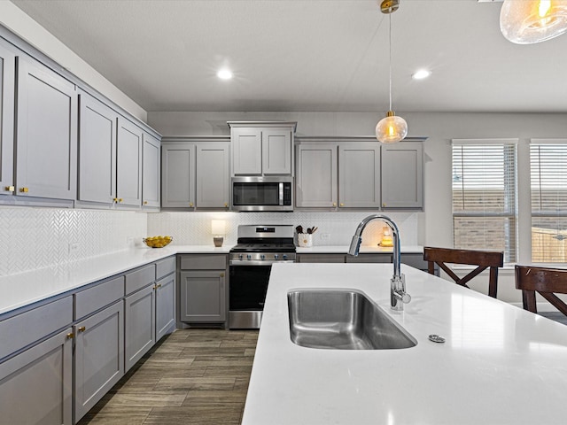 kitchen with decorative backsplash, gray cabinets, stainless steel appliances, light countertops, and a sink