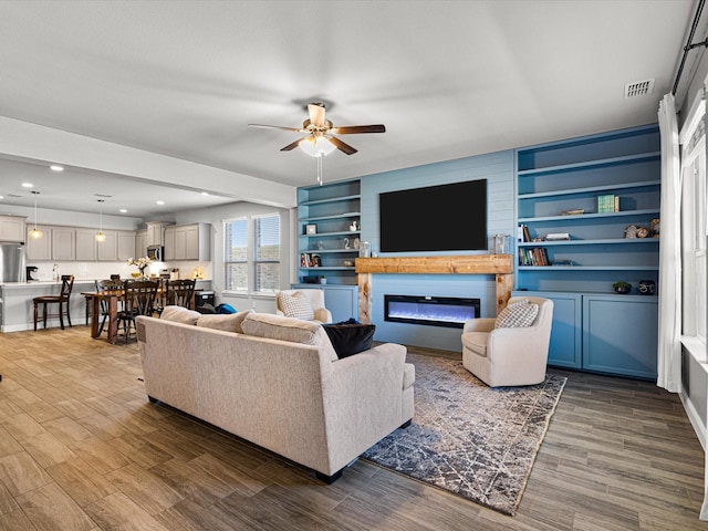 living room featuring a ceiling fan, visible vents, wood finished floors, and a glass covered fireplace