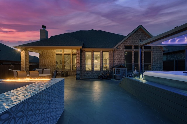 back of property at dusk featuring an outdoor living space with a fire pit, a patio area, brick siding, and a chimney