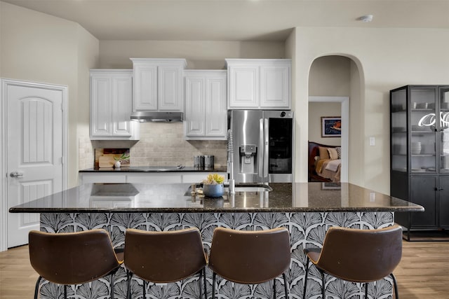 2822 Palmerston Dr, Midlothian, TX 76065 - kitchen with stainless steel fridge, light wood-style flooring, under cabinet range hood, tasteful backsplash, and a center island with sink