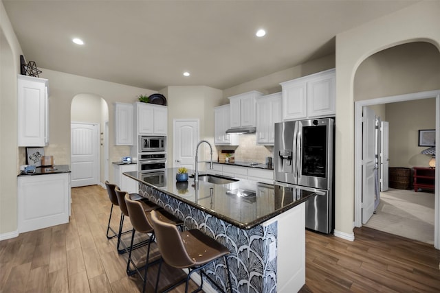 2822 Palmerston Dr, Midlothian, TX 76065 - kitchen with appliances with stainless steel finishes, arched walkways, under cabinet range hood, wood finished floors, and backsplash
