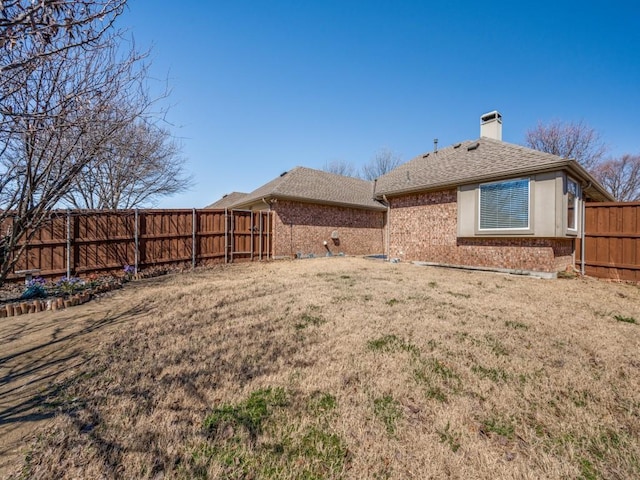 rear view of property featuring a fenced backyard, brick siding, roof with shingles, a lawn, and a chimney