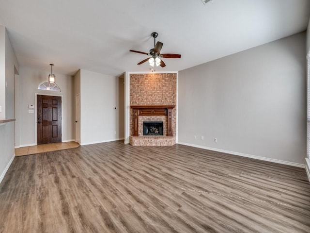 unfurnished living room with a brick fireplace, wood finished floors, a ceiling fan, and baseboards