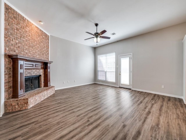 unfurnished living room featuring baseboards, visible vents, ceiling fan, wood finished floors, and a brick fireplace