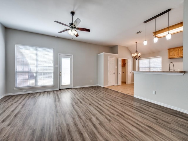 unfurnished living room with wood finished floors, a sink, baseboards, and ceiling fan with notable chandelier