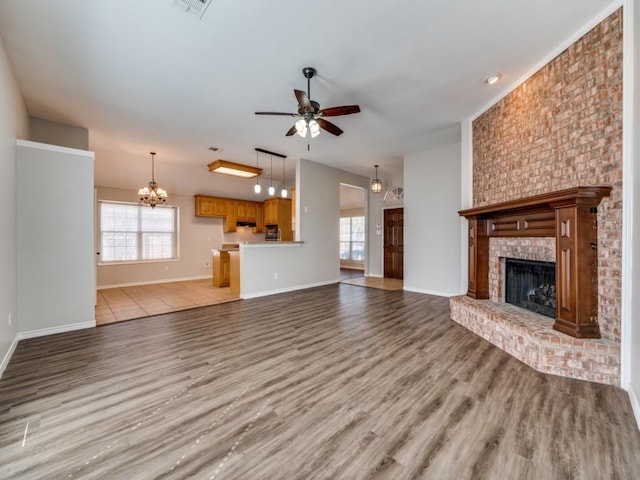 unfurnished living room featuring visible vents, baseboards, light wood-style floors, a brick fireplace, and ceiling fan with notable chandelier